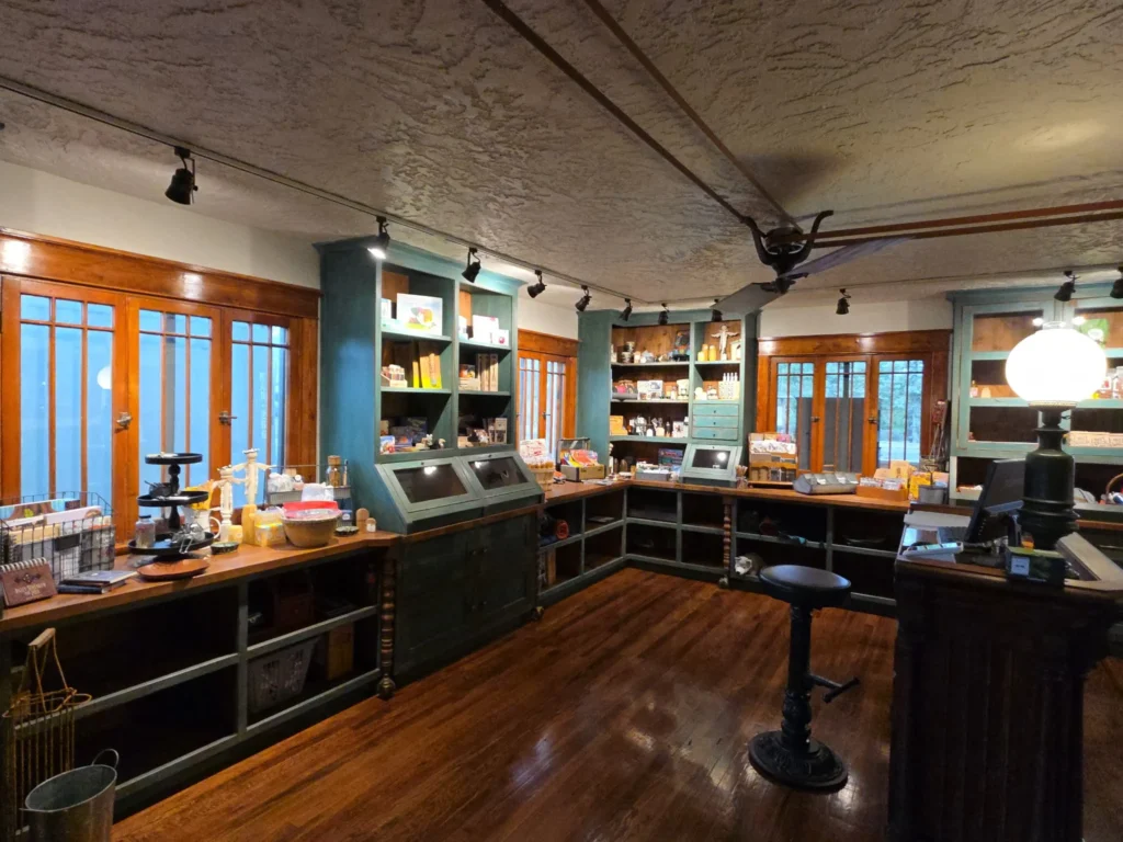 A vintage-style store interior with wooden floors, shelves stocked with assorted goods, and warm lighting evokes the charm of a historic chama hotel. An empty stool sits near the counter, inviting you to linger.